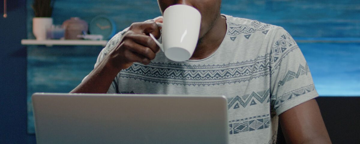 Man working from home in front of a computer and drinking from a mug